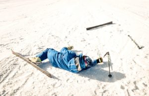 a person in a blue suit lying on snow with a ski injury